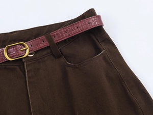 Dettaglio pantaloni marroni con cintura in coccodrillo rosso-marrone e fibbia dorata