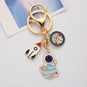 Golden astronaut keychain with enamel rocket and planet charms on white background