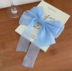Close-up of light blue organza bow hair clip with long ribbons on a vintage book