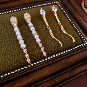 Elegant gold snake-shaped earrings with zircon and pearls on green velvet background