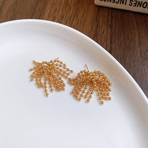 Macro detail of gold-plated beaded tassel earrings on a minimalist white ceramic tray