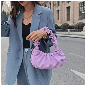 Detail of a purple pleated cloud handbag held by a model in a blue blazer