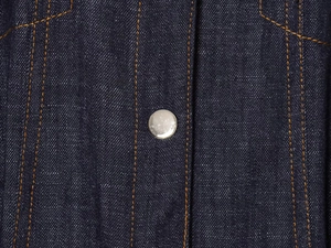 Close-up of dark blue denim fabric with silver metal button and yellow double stitching