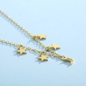 Macro detail of gold star and crescent moon pendants with inset crystals on a chain