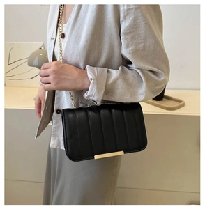 Detail of black leather crossbody bag featuring gold chain strap and quilted texture style