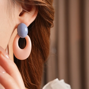 Close-up of stylish blue and pink oval resin drop earrings worn by a female model