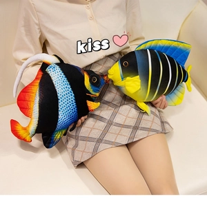 Detail of colorful plush tropical fish pillows held by model on white sofa
