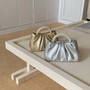 Chic gold and silver pleated cloud bags with elegant pearl handles on a display stand