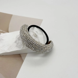 Close-up of golden alloy ponytail cuff encrusted with rhinestones on white marble stand