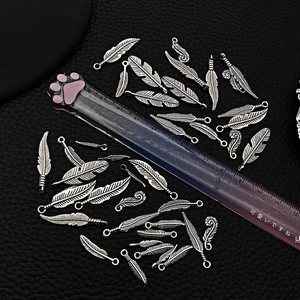 Macro shot of vintage silver alloy feather charms on black leather with a size ruler