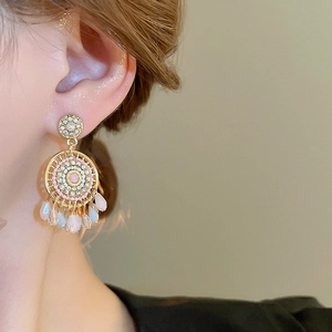 Close-up of bohemian dreamcatcher gold tassel earrings with pink pearls worn by a model