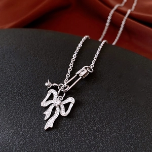 Macro view of silver bow necklace with zircon pavé and orb charm on red satin backdrop
