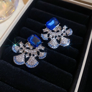 Macro shot of silver fan-shaped earrings with blue square gems in a black velvet box