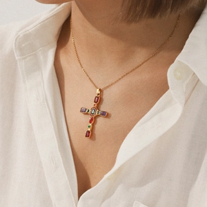 Close-up of golden cross necklace with colorful zircon stones worn on model's neck