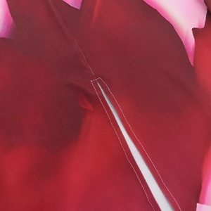 Dettaglio di vestito floreale rosso con cuciture di precisione sul bordo dello spacco
