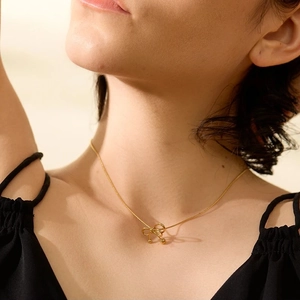 Dettaglio ravvicinato di una collana dorata con ciondolo a fiocco su una modella