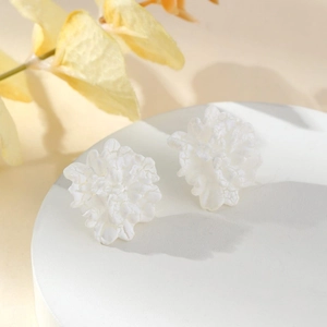 Detail shot of white double-petal flower stud earrings on a minimalist white stand