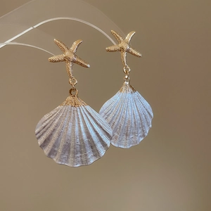 Macro detail of starfish earrings with white shell pendants and golden trim for beach style