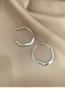 Close-up of irregular silver hoop earrings on champagne silk fabric with soft lighting