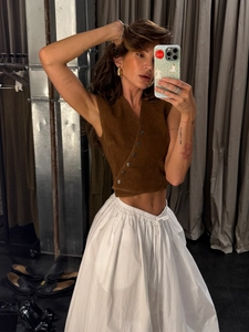 Detail of a brown suede button-up vest paired with white cotton linen maxi skirt with drawstring