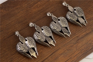 Gros plan de quatre pendentifs ailes de cœur en argent avec détails de flèche sur bois