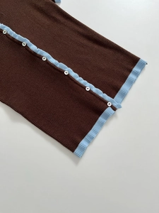 Close-up of slim knit top featuring contrast blue ruffled edges and white buttons
