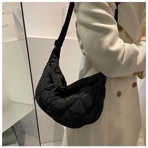 Detail view of the black quilted nylon crescent crossbody bag worn by a model