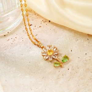 Détail d'un pendentif tournesol doré avec pierre centrale jaune et pétales en zircon