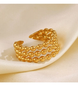 Détail d'une bague à trois couches de perles dorées sur un tissu en soie champagne