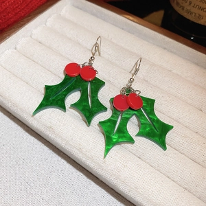 Festive holly leaf drop earrings in green and red finish on a cream velvet tray