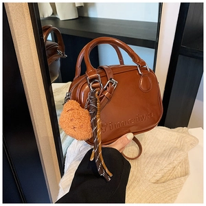 Detail of caramel brown crossbody bag with plush bear charm and woven tassel accent