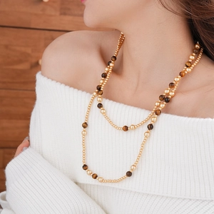 Detail of layered faux tiger eye and gold bead long necklace on white knitwear