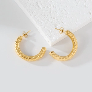 Détail de boucles d'oreilles créoles dorées en C avec texture métal martelé irrégulière