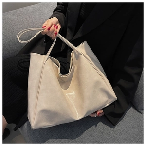 Close-up of minimalist cream PU leather tote bag held by model in black blazer