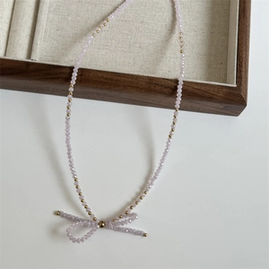 Close-up of light purple faceted crystal beads with a woven bow pendant on wood