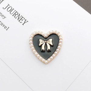 Detail of a vintage black heart charm with a golden bow and pearl edges on a white card