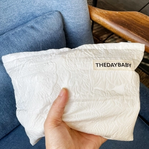 Close-up of hand holding a white floral jacquard fabric cosmetic bag with branding label