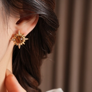Detail of vintage sunburst earring with tiger eye stone and zircon on female ear