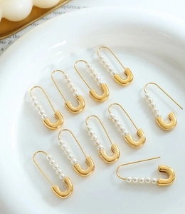 Macro detail of paperclip-shaped gold earrings with white pearls on a ceramic plate