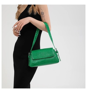 Close-up of green crocodile pattern handbag with wide shoulder strap on model in black dress