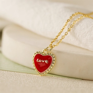 Detailansicht einer Goldkette mit rotem Herzanhänger und eingraviertem Love-Schriftzug