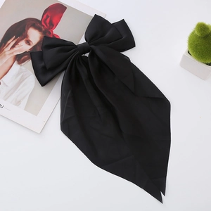 Close-up of elegant black satin bow hair clip with long ribbons on a white surface