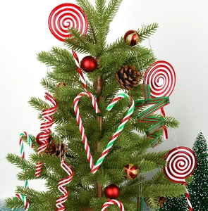 Close-up of red and white candy cane ornaments hanging on a green Christmas tree