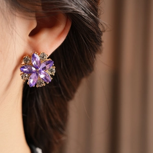 Dettaglio di orecchini vintage a fiore viola con cristalli su orecchio di modella
