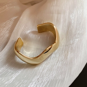 Macro di un bracciale rigido dorato a onde posato su un elegante tessuto di seta bianca