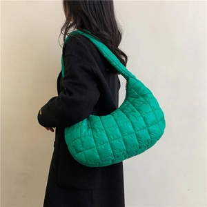 Minimalist green quilted crescent shoulder bag shown on model with chic black coat