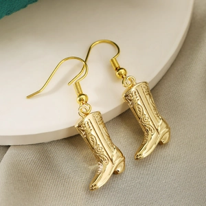 Golden Western cowboy boot earrings with hook closure on a minimalist pedestal