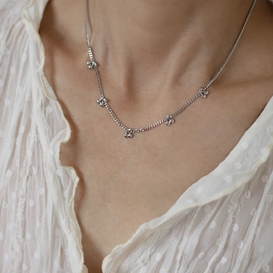 Close-up of a silver cherry pendant necklace worn by a model on a white lace top