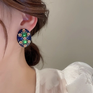 Close-up of vintage style green square gemstone earrings with gold floral patterns