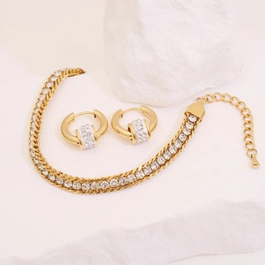 Detail shot of gold-plated bracelet and earrings set with crystal pave on stone surface